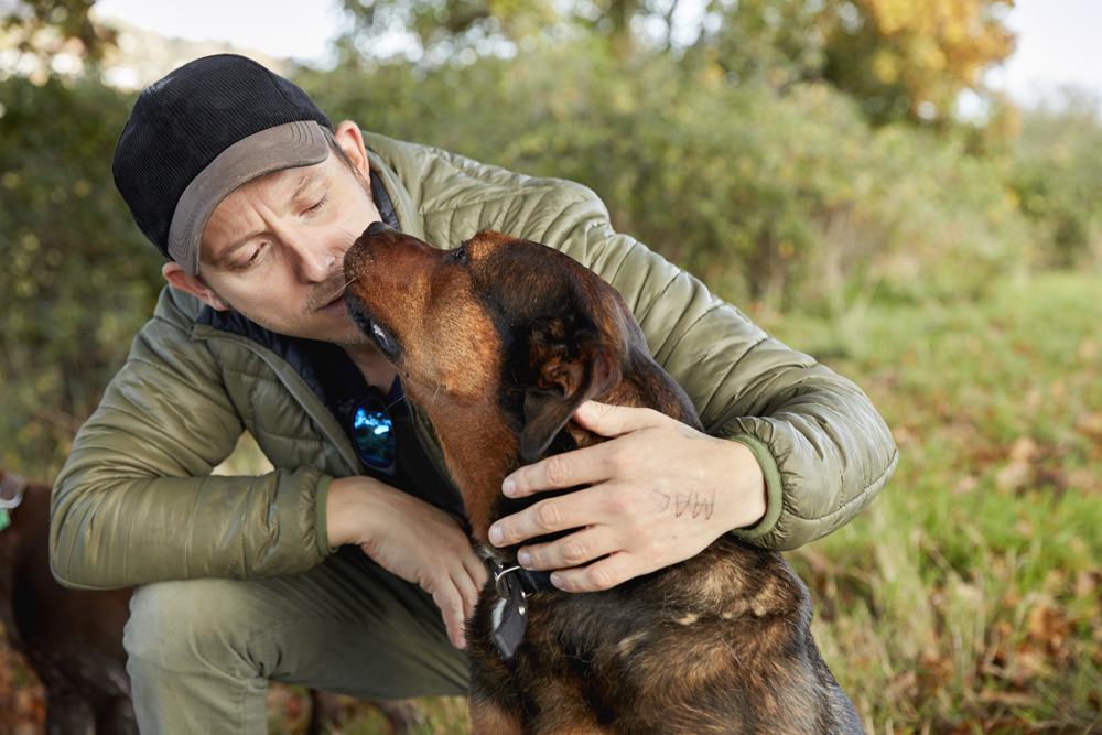 A man embracing his dog in a grassy field